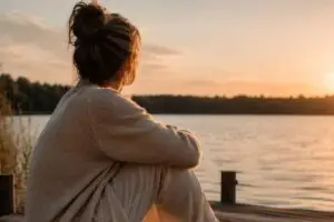 Vrouw zit bij zonsondergang aan het water en ervaart rust als beeld voor veilige hechting opbouwen als volwassene
